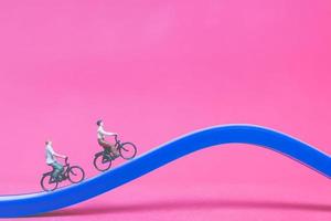Viajeros en miniatura con bicicletas en un puente azul sobre un fondo de color rosa