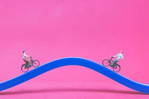 Viajeros en miniatura con bicicletas en un puente azul sobre un fondo de color rosa foto