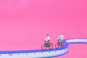 Viajeros en miniatura con bicicletas en un puente azul sobre un fondo de color rosa foto