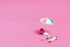 Miniature people wearing swimsuits relaxing on a pink background photo