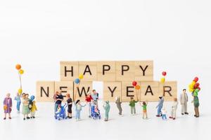 Familias en miniatura sobre bloques de madera con el texto feliz año nuevo sobre un fondo blanco. foto