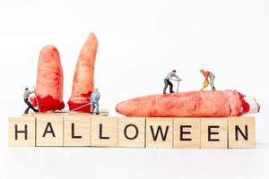 Trabajadores en miniatura que se unen para crear accesorios de fiesta de Halloween con bloques de madera con el texto Halloween sobre un fondo blanco. foto