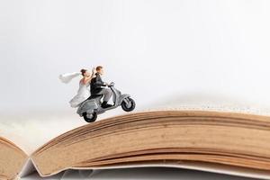 Miniature couple riding a motorcycle on an old book, Valentine's Day concept photo