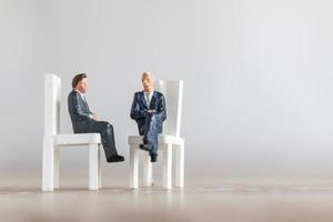 Miniature businesspeople sitting on chairs with a blurred background photo