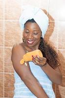 Young woman applying body lotion after bath photo