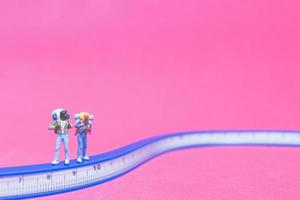 Pareja de viajeros en miniatura en un puente con un fondo de color rosa foto