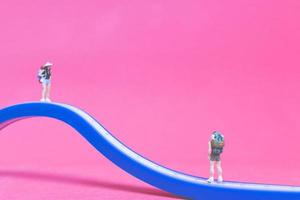 Miniature couple of travelers on a bridge with a pink background photo