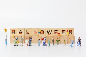 Miniature people holding balloons with wooden blocks with text Halloween on a white background