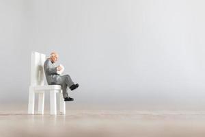 Miniature businessman reading a book on a chair, education and business concept photo