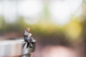 Miniature businessman sitting and reading a book outdoors, education and business concept photo