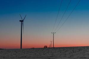 Wind power plant in the field next to a power line at sunset