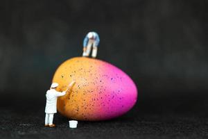 Miniature people painting Easter eggs for Easter day on a black background photo