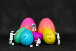 Miniature people painting Easter eggs for Easter day on a black background photo