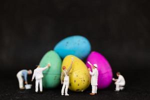 Miniature people painting Easter eggs for Easter day on a black background photo