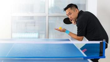 Macho jugando tenis de mesa con raqueta y pelota en un pabellón deportivo foto