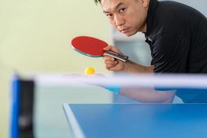 Macho jugando tenis de mesa con raqueta y pelota en un pabellón deportivo foto