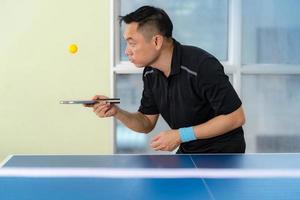 Macho jugando tenis de mesa con raqueta y pelota en un pabellón deportivo foto