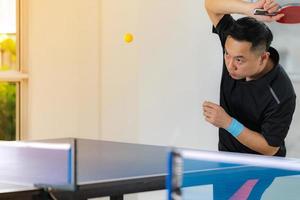 Macho jugando tenis de mesa con raqueta y pelota en un pabellón deportivo foto