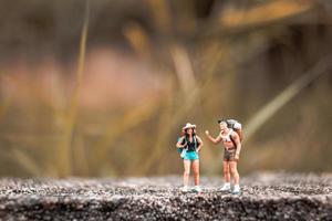 Miniature backpackers standing on a concrete floor with a bokeh nature background photo