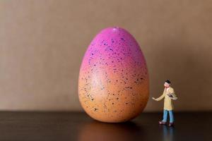 Miniature artist holding a brush and painting Easter eggs for Easter
