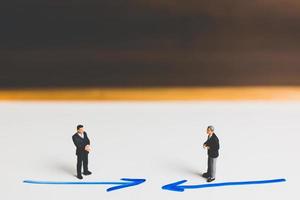 Miniature businessmen standing on an arrow pathway, business decision concept photo