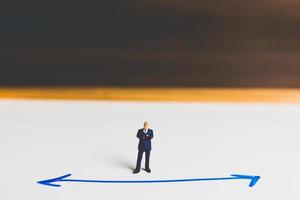 Miniature businessman standing on an arrow pathway, business decision concept