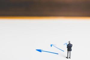 Miniature businessman standing on an arrow pathway, business decision concept