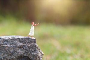 Miniature sleepy woman suffering from somnambulism on a rock cliff with a nature background photo