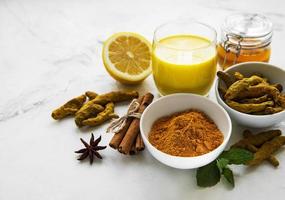 Golden milk with cinnamon, turmeric, ginger and honey over white marble background photo