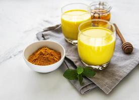 Golden milk with cinnamon, turmeric, ginger and honey over white marble background photo