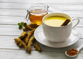 Leche dorada con canela, cúrcuma, jengibre y miel sobre fondo de madera blanca foto