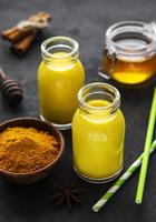 Golden milk with cinnamon, turmeric, ginger and honey over black concrete background photo