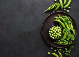 Green peas in a bowl with fresh pods on the black concrete background photo