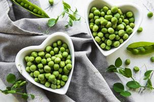 Green peas in heart shaped bowls on a fabric background photo