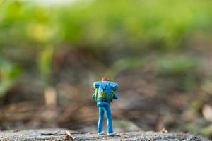 Viajero en miniatura con una mochila caminando en un prado, concepto de viaje y aventura foto