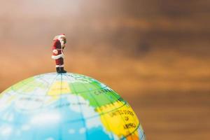 Miniature Santa Claus carrying gifts standing on a globe photo