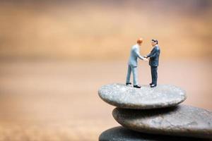 Miniature businessmen standing on a stone, challenges and risks concept photo