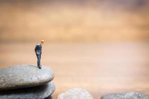 Empresario en miniatura de pie sobre una piedra, concepto de desafíos y riesgos foto