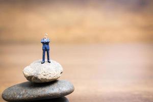 Empresario en miniatura de pie sobre una piedra, concepto de desafíos y riesgos