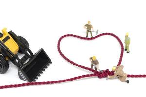 Trabajadores en miniatura construyendo una cuerda en forma de corazón sobre un fondo blanco. foto
