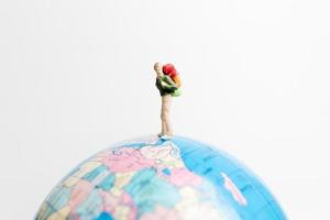 Miniature person standing on a globe with a white background, travel concept photo