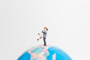 Gente en miniatura de pie sobre un globo terráqueo con un fondo blanco, concepto de viaje foto