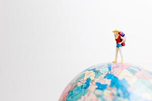 Miniature person standing on a globe with a white background, travel concept photo