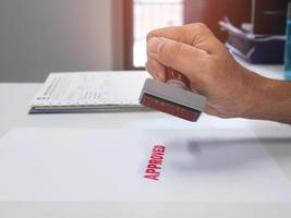 Hand using a stamp with the word approved at an office desk with papers photo