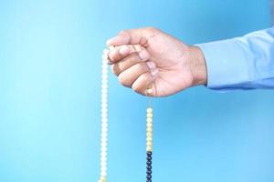 Muslim man's hand holding prayer beads on blue background
