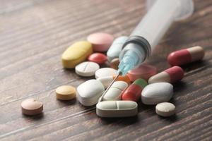 Syringe and pills on wood background, close up photo
