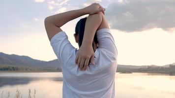 Una mujer asiática estirando antes de correr por el lago. video