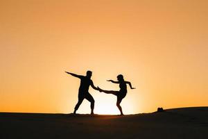 Silhouettes of a happy young couple on a background of orange sunset in the sand desert