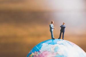 Miniature businessmen standing on a globe world map with a brown background photo