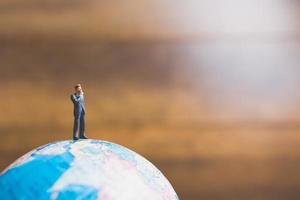 Empresario en miniatura de pie sobre un mapa del mundo globo con un fondo marrón